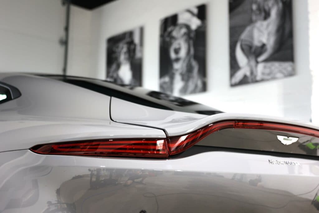 Close-up of a polished Aston Martin rear tail light inside a professional auto detailing shop in Purcellville